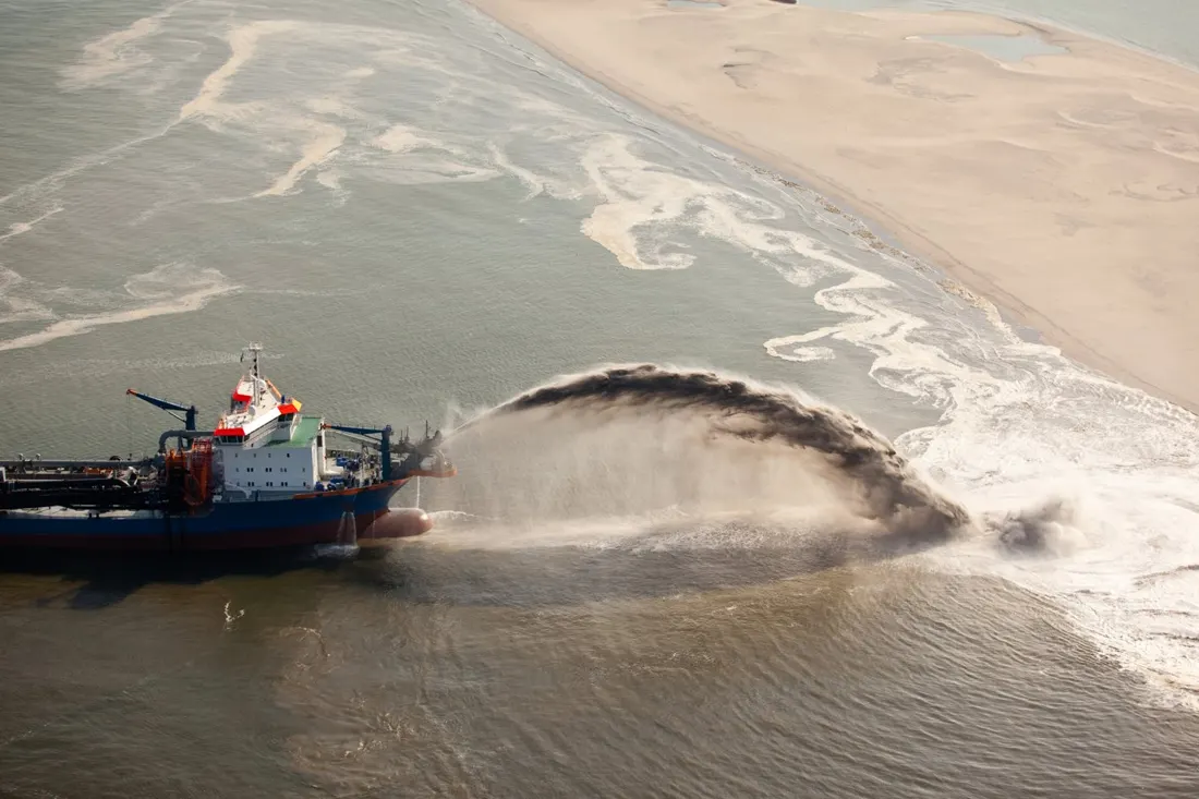 Aerial view of a hopper dredger rainbowing sand onto a newly formed coastline