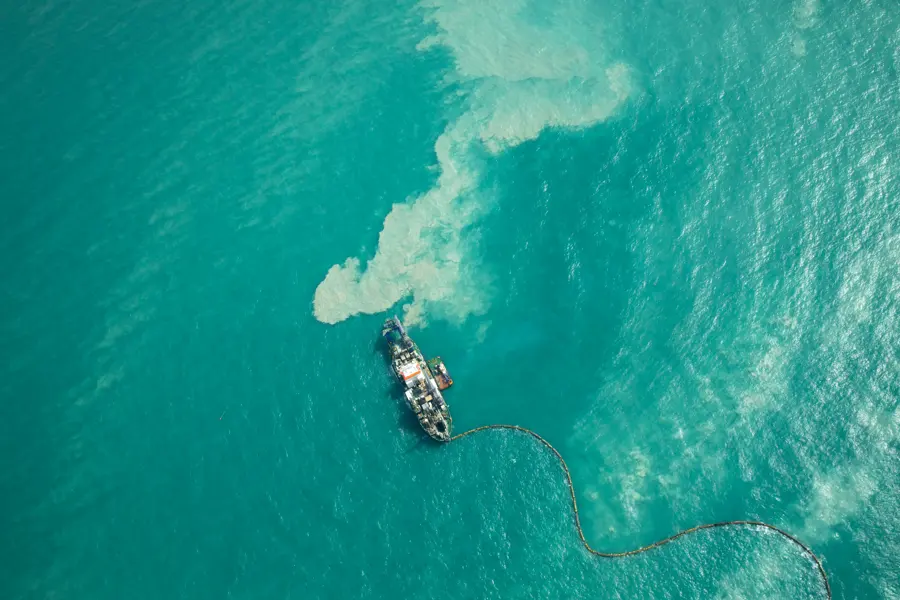 Aerial view of a dredging vessel dispersing sediment into turquoise coastal waters