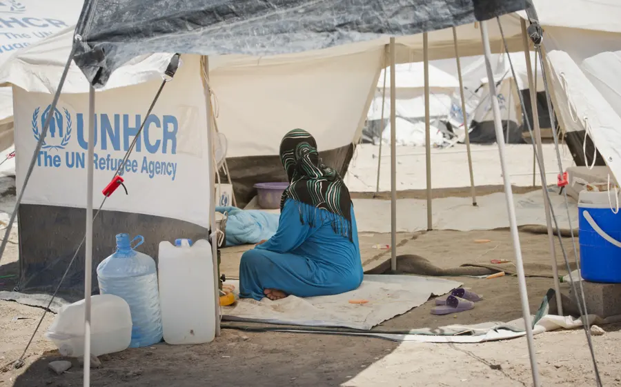 A woman seated beside water containers and a tent