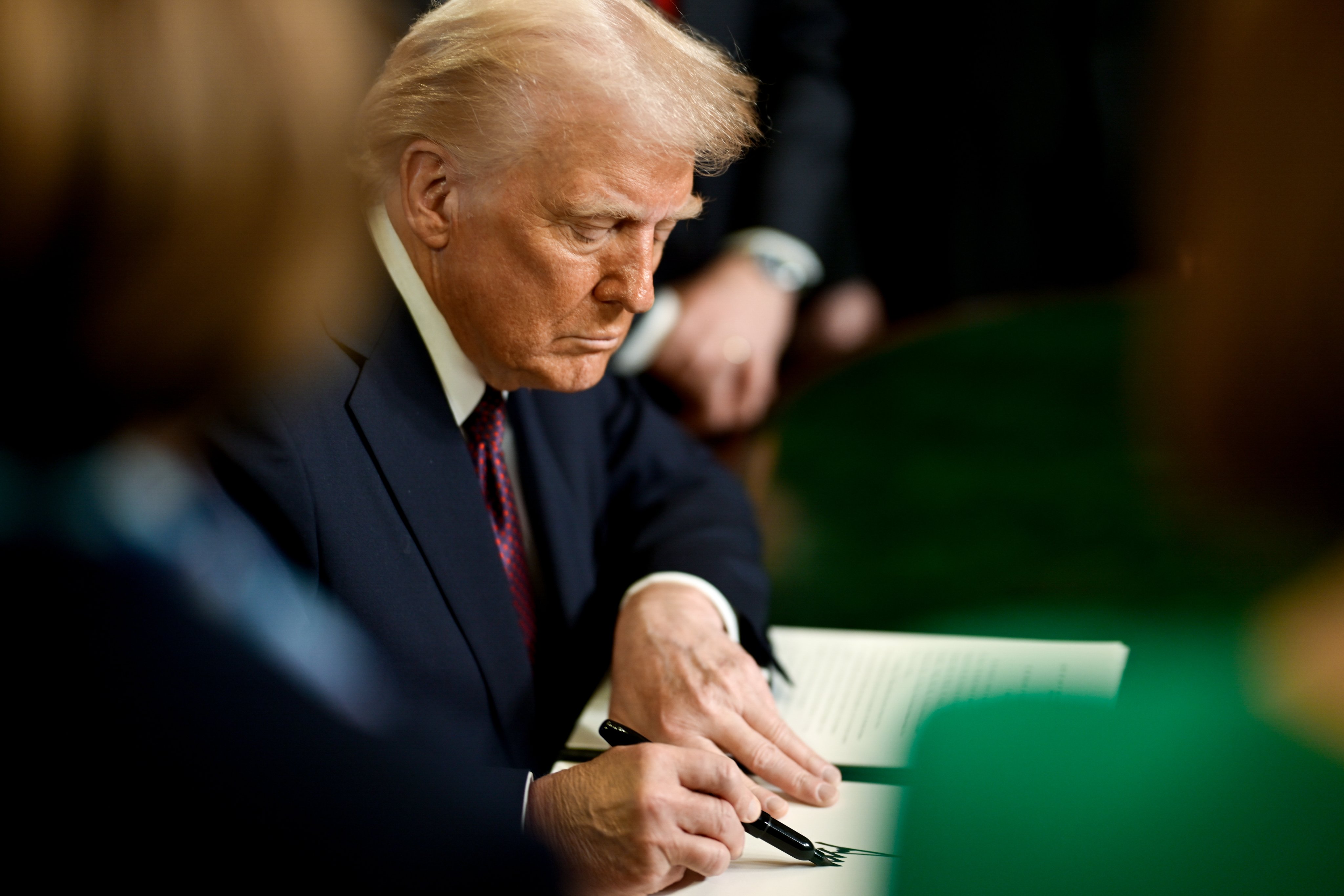 President Donald Trump signing a document at the Resolute Desk in the Oval Office